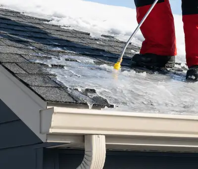 Ice dam removal technician using a steam wand to melt thick ice buildup on a residential roof in Allentown, PA