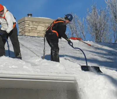 Professional technicians performing roof snow removal with safety harnesses and shovels in Allentown, PA